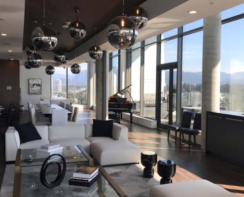 Modern living room with large windows, white sofas, glass coffee table, black decorative items, hanging orb lights, and a grand piano. Mountain and city views are visible through the windows.