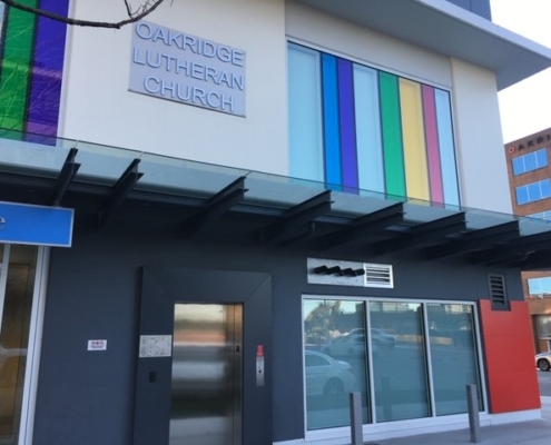 The exterior of Oakridge Lutheran Church, featuring a sign and colorful vertical panels above the entrance, with large windows and a modern design.